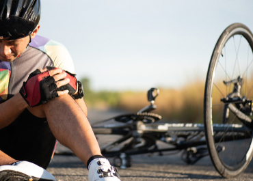 Injured cyclist clutching his knee next to his fallen bicycle on the road.