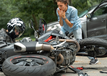 Injured motorcycle rider and a worried woman next to a crashed bike.