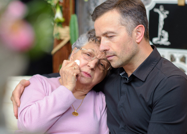 A comforting man embracing an older woman who is crying.