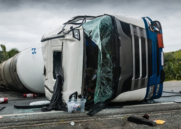 Large semi-truck overturned on the highway with a shattered windshield.