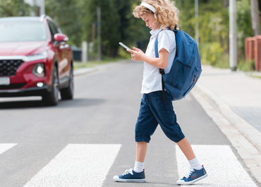 Child looking at a phone while walking in a crosswalk as a car approaches.