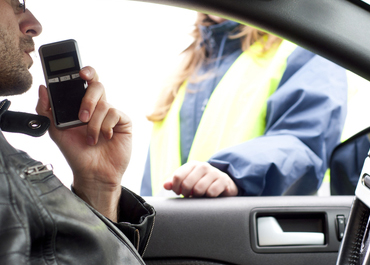 Driver breathing into a breathalyzer held by a police officer.