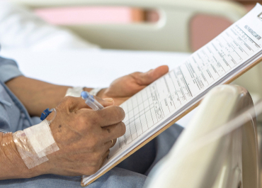 Injured patient in a hospital bed filling out compensation forms.