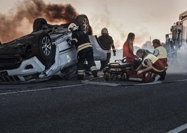 First responders assisting injured people next to an overturned car after a serious accident.
