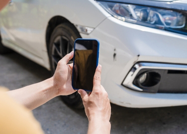 Person using a phone to photograph damage on a white car after an accident.