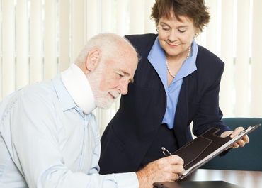 Elderly man with a neck brace consults with a female attorney about a document. Title: How Attorneys Maximize PI Settlements.