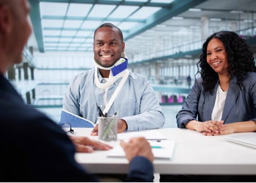 Black man in a neck brace meeting with two personal injury lawyers. Title: Preparing For Your First Meeting With A Personal Injury Lawyer.
