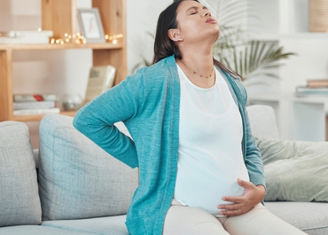 Pregnant woman experiencing severe back pain on a couch. title: Understanding Legal Options For Birth Injuries.