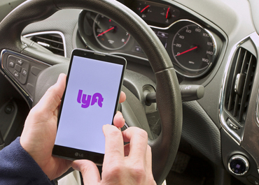 Close-up of a person holding a smartphone displaying the Lyft app logo. Title: The Legal Process After A Lyft Accident.