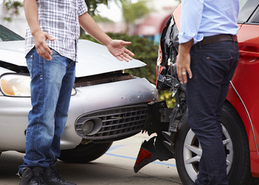 Two men inspecting the front-end damage of their cars after an accident. Title: How To Determine Fault In A Car Accident.