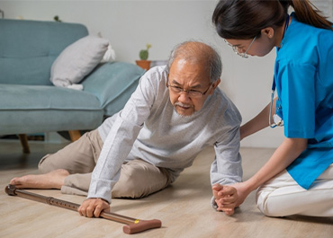 An elderly man who has fallen on the floor is being helped by a caregiver. Title: Tips For Property Owners To Prevent Falls.