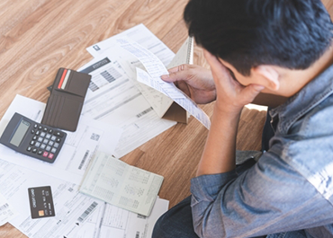 Frustrated person with head in hands looking at financial documents, calculator, and credit cards. Title: Signs A Business May Need To File Bankruptcy.