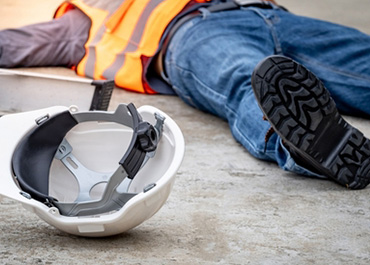 Construction worker lying injured on the ground with a hard hat nearby. Title: Legal Options After A Construction Injury.
