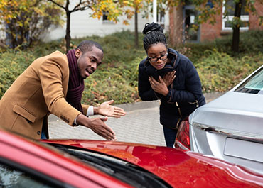 Two people checking the damage on a car after an accident. Title: Top 10 Questions To Ask Before Hiring A Car Accident Lawyer.